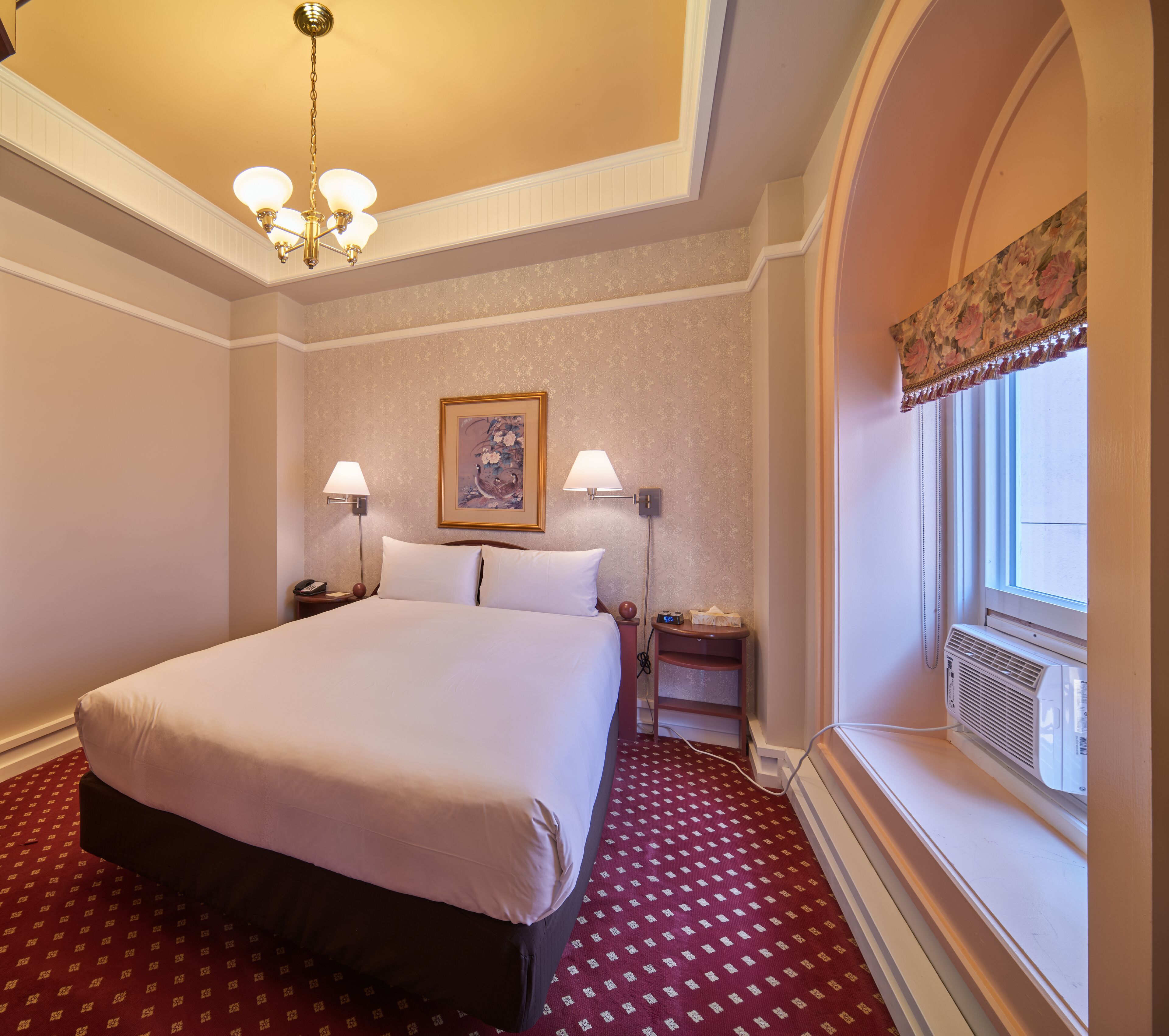 Habitación de hotel con una cama grande, dos mesitas de noche con lámparas, un cuadro en la pared y una ventana con vistas.