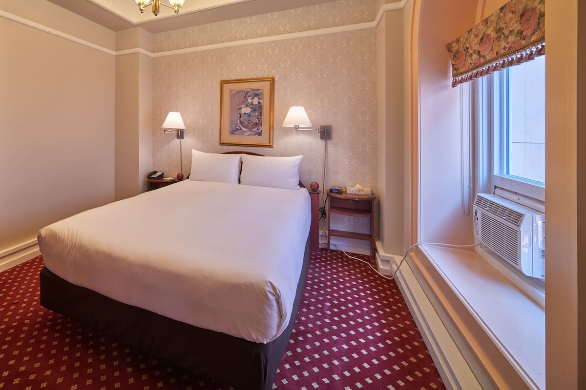 A hotel room with a large bed, two bedside tables with lamps, a painting on the wall, and a window with a view.