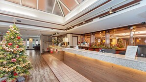 A hotel lobby with a Christmas tree, a reception desk, and a large window overlooking the lobby. - Bedford Regency Hotel, Trademark Collection by Wyndham (Victoria)