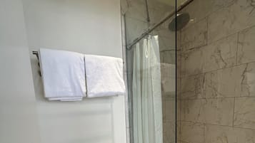 A bathroom with a toilet, a glass shower enclosure, and a marble-tiled wall.
