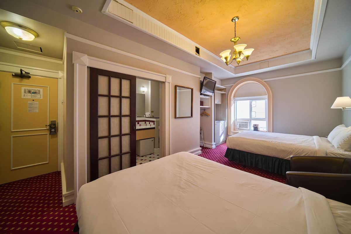 A hotel room with two beds, a bathroom, a mirror, and a chandelier.