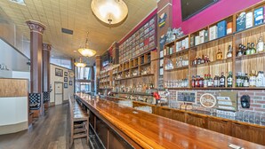 A bar area with wooden bar counters, shelves of liquor bottles, and a menu board. - Bedford Regency Hotel, Trademark Collection by Wyndham (Victoria)