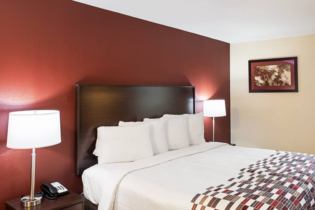 A hotel room with a large bed, a nightstand with a lamp and phone, and a framed picture on the wall.
