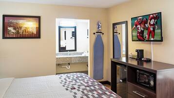 A hotel room with a bed, a desk with a microwave, a coffee maker, and a TV on the wall.