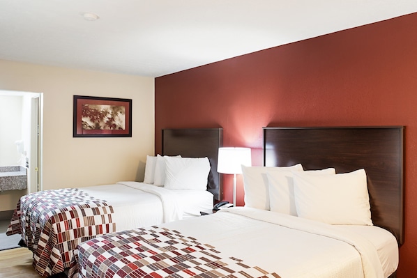 A hotel room with two beds, a wooden headboard, a framed picture on the wall, and a bedside lamp. - Red Roof Inn Indianapolis East (Indianapolis)