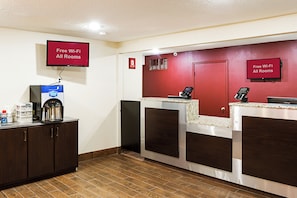 A hotel reception area with a coffee machine, a digital screen, and a sign indicating free Wi-Fi in all rooms. - Red Roof Inn Indianapolis East (Indianapolis)