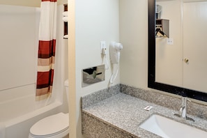 A bathroom with a toilet, a shower curtain, a hairdryer, and a sink with a mirror. - Red Roof Inn Indianapolis East (Indianapolis)