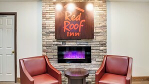 A Red Roof Inn sign above a fireplace, two leather chairs, and a small round table. - Red Roof Inn Indianapolis East (Indianapolis)