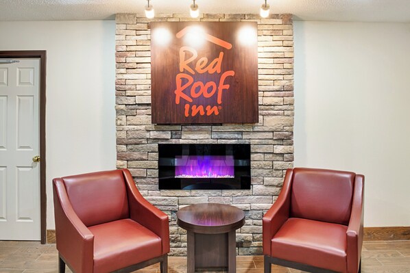 A Red Roof Inn sign above a fireplace, two leather chairs, and a small round table.