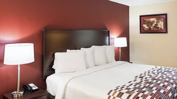 A hotel room with a bed, two bedside lamps, a telephone, and a framed picture on the wall. - Red Roof Inn Indianapolis East (Indianapolis)