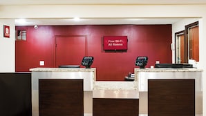 A reception desk with a red wall, a closed door, and a sign indicating free Wi-Fi in all rooms. - Red Roof Inn Indianapolis East (Indianapolis)