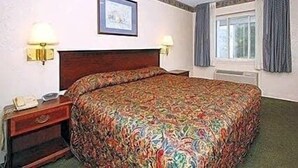 Une chambre d’hôtel avec un grand lit, deux tables de chevet, une petite table, un tableau encadré au mur et une fenêtre avec des rideaux.