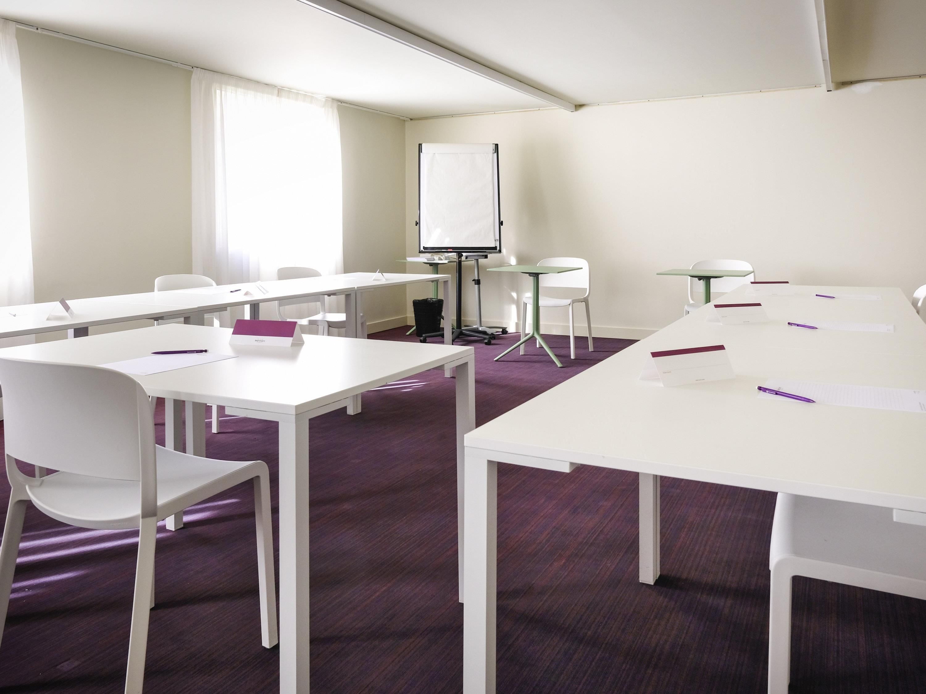 Un salón de conferencias con mesas blancas, sillas, una pizarra y un proyector.
