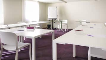 Un salón de conferencias con mesas blancas, sillas, una pizarra y un proyector.