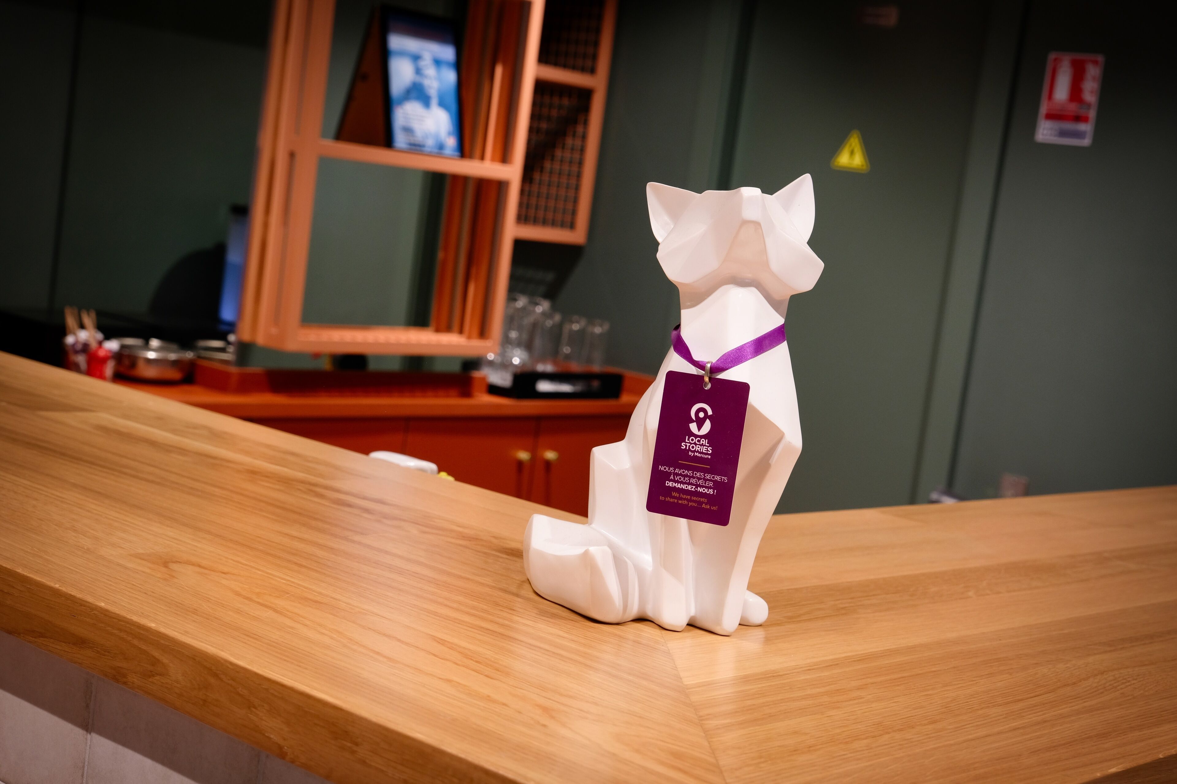 Une statuette de chat blanc avec un ruban violet, posée sur un comptoir en bois.