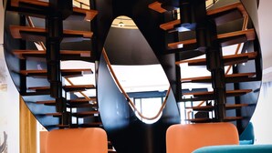 A modern interior with a spiral staircase, orange and teal seating, and a geometric floor pattern. - Mercure Perpignan Centre (Perpignan)
