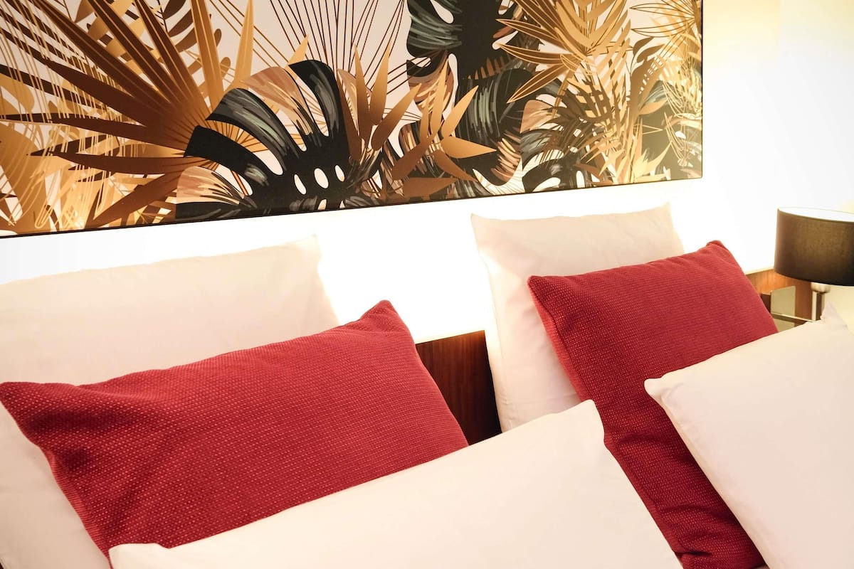A hotel room with a bed, two pillows, a nightstand, and a wall art piece.