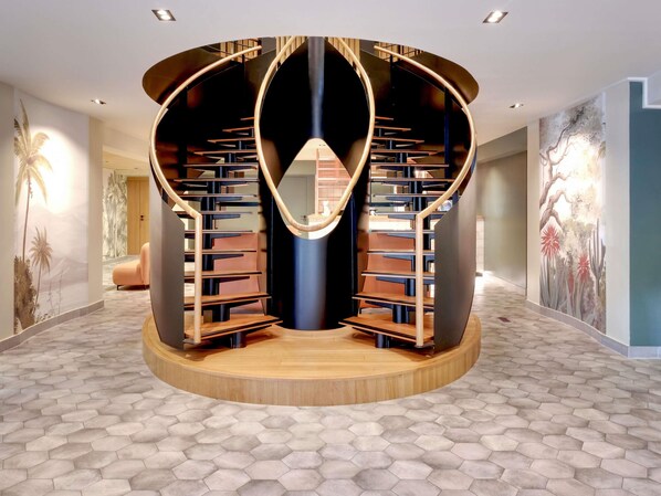 A circular staircase with a central open space, surrounded by bookshelves, in a modern interior with hexagonal patterned flooring.