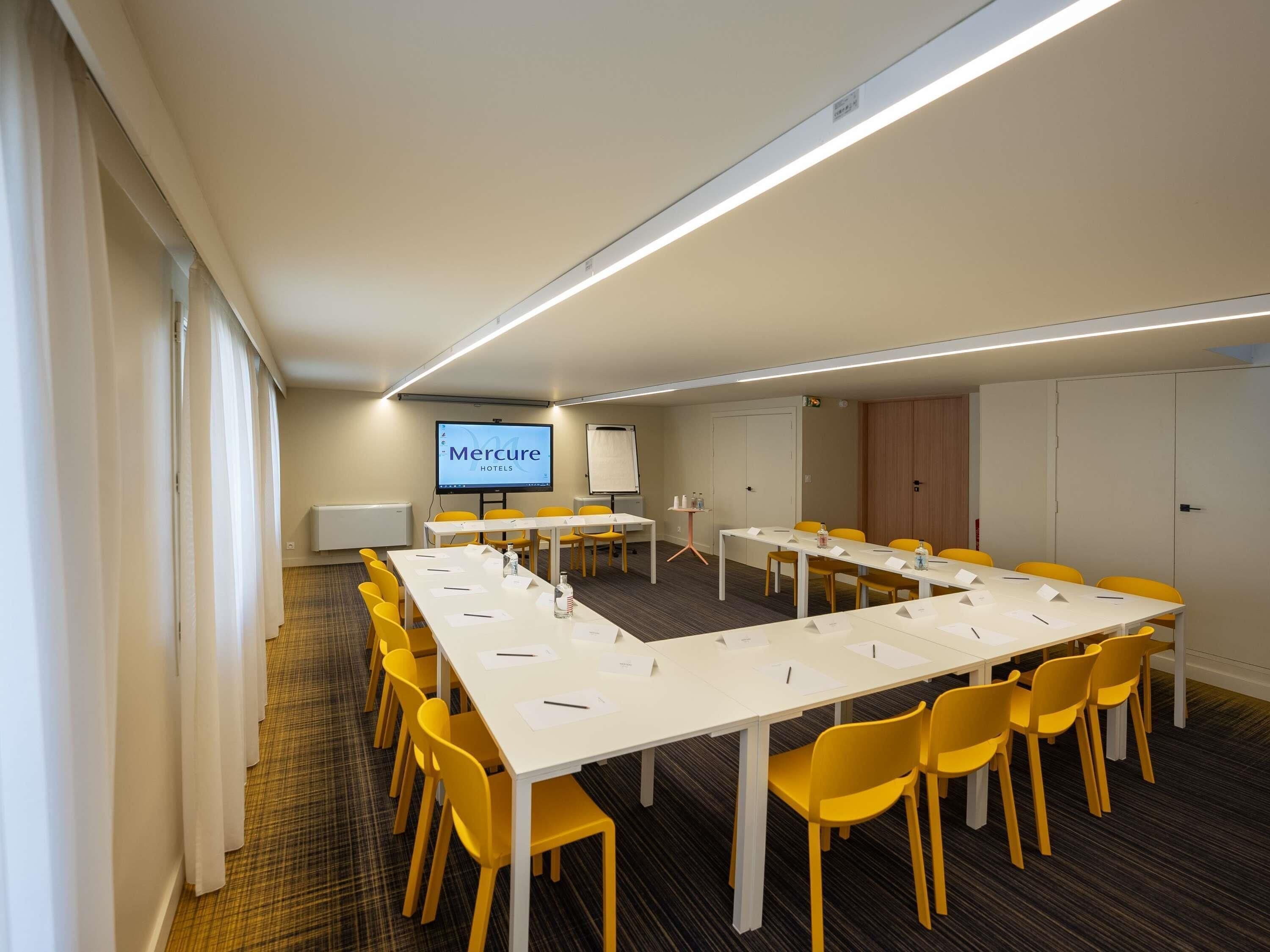 Una sala de conferencias con una larga mesa, sillas amarillas, una pantalla de proyección y una pizarra.