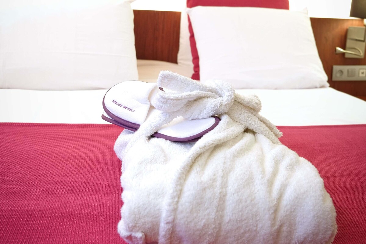 A hotel room with a bed, pillows, a robe, and slippers.