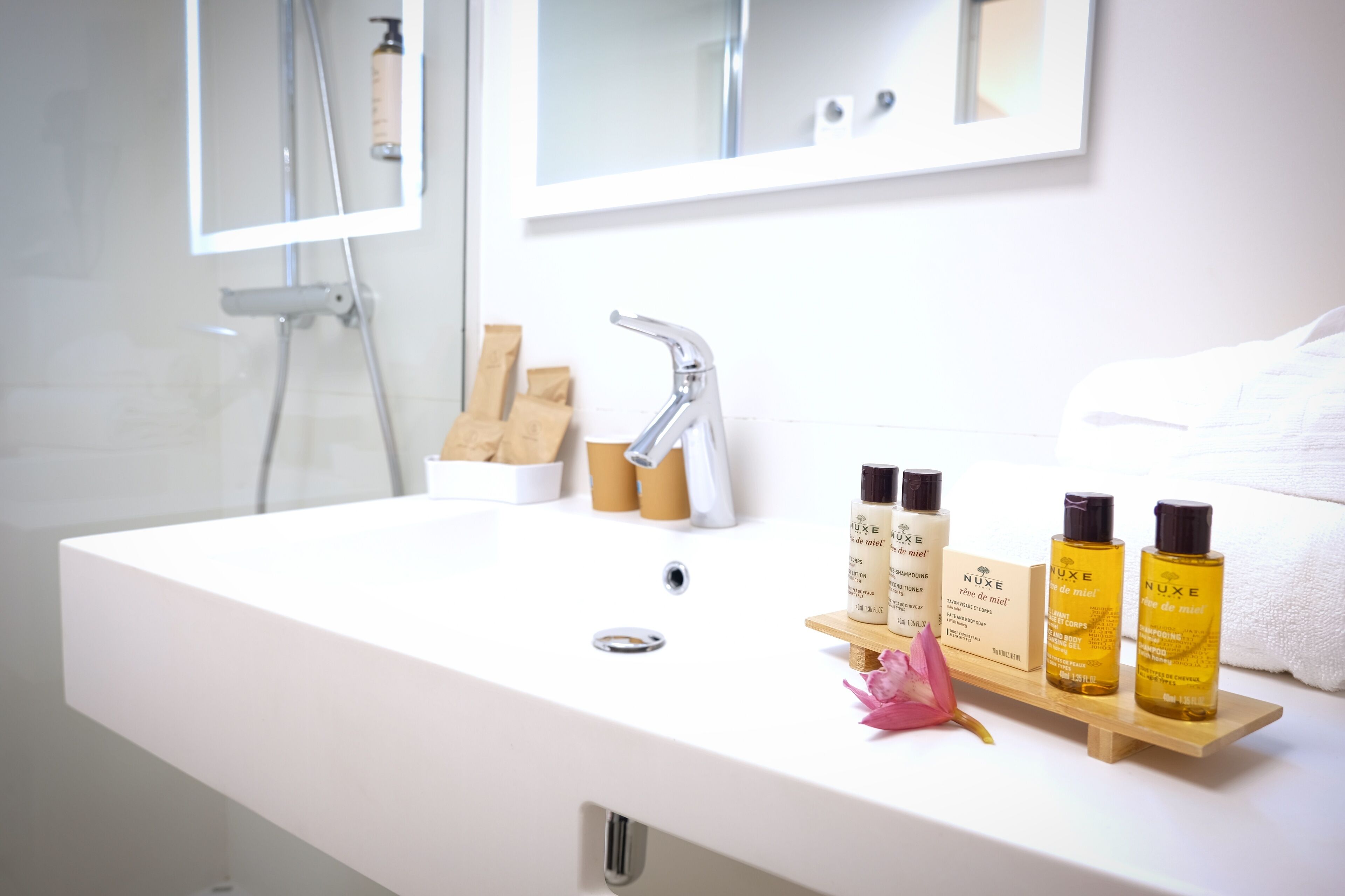 A bathroom with a white sink, a mirror, and toiletries on a wooden tray.