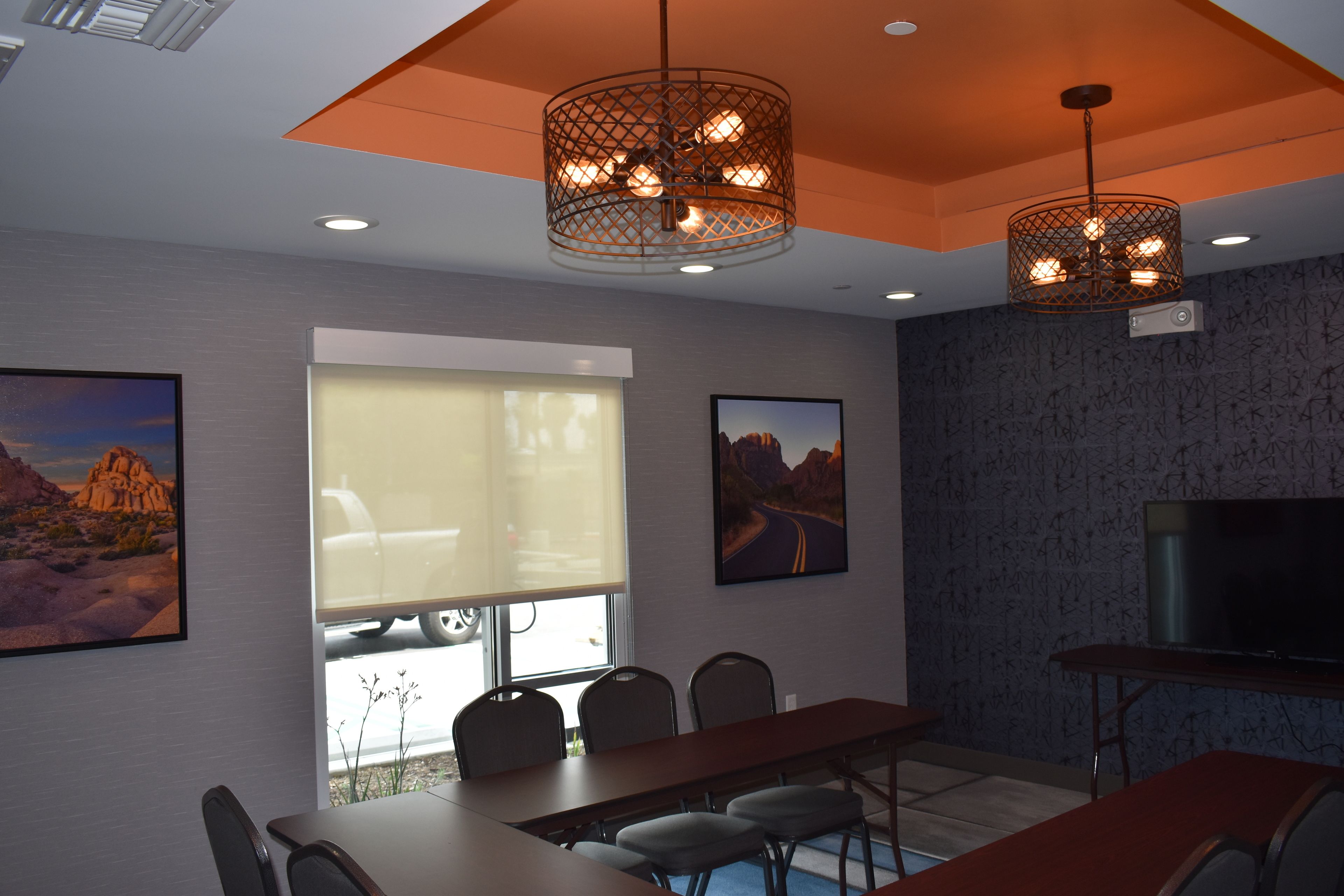 A conference room with a long table, chairs, a TV, and two pendant lights.