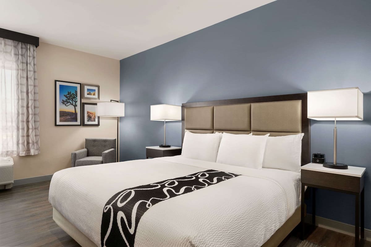 A hotel room with a large bed, two bedside tables, a chair, and a window with curtains.