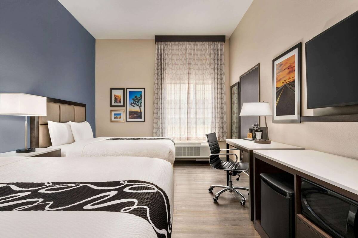 A hotel room with two beds, a desk, a chair, and a TV.