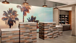 Un área de recepción de diseño moderno, con un mural de palmeras y una cita inspiradora. Hay dos mostradores de recepción con un diseño tipo ladrillo.