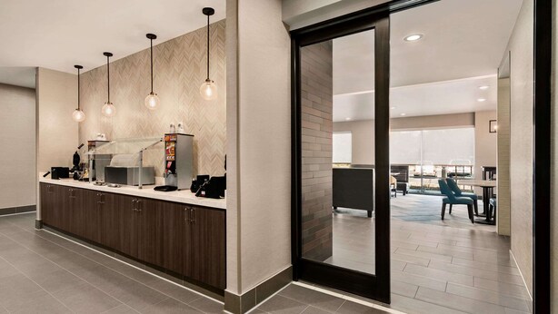 Un moderno vestíbulo de hotel con un mostrador de recepción, iluminación colgante y vistas al comedor.