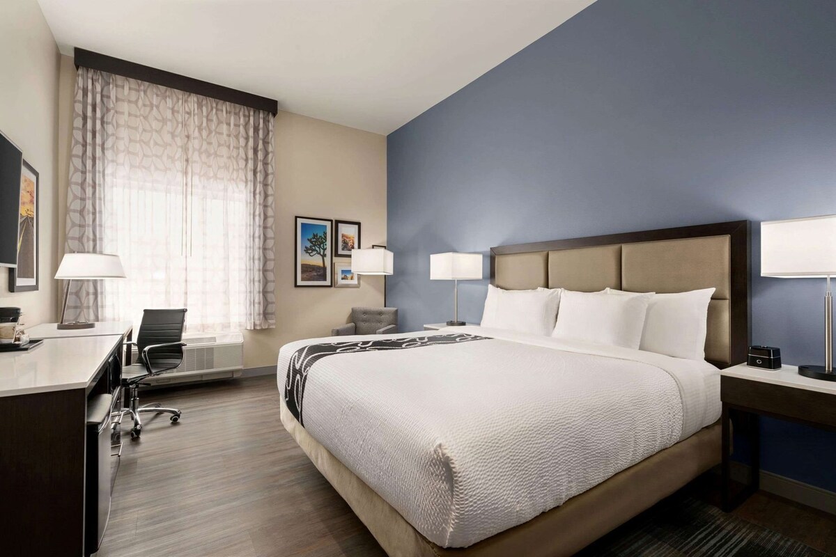 Una habitación de hotel con cama, escritorio, silla y dos lámparas de noche.