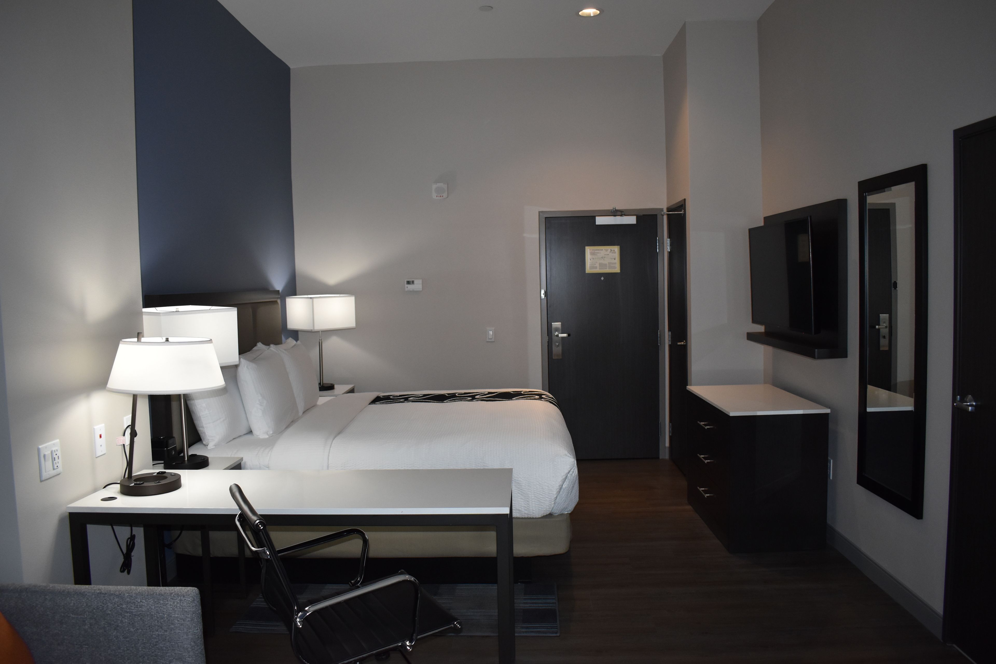 Une chambre d’hôtel comprenant un lit, des lampes de chevet, un bureau avec une chaise, une commode et un téléviseur fixé au mur.