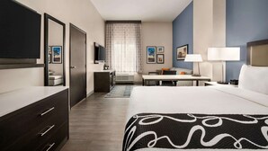 Habitación de hotel con una cama grande, un escritorio, un televisor, un armario y una ventana con cortinas.