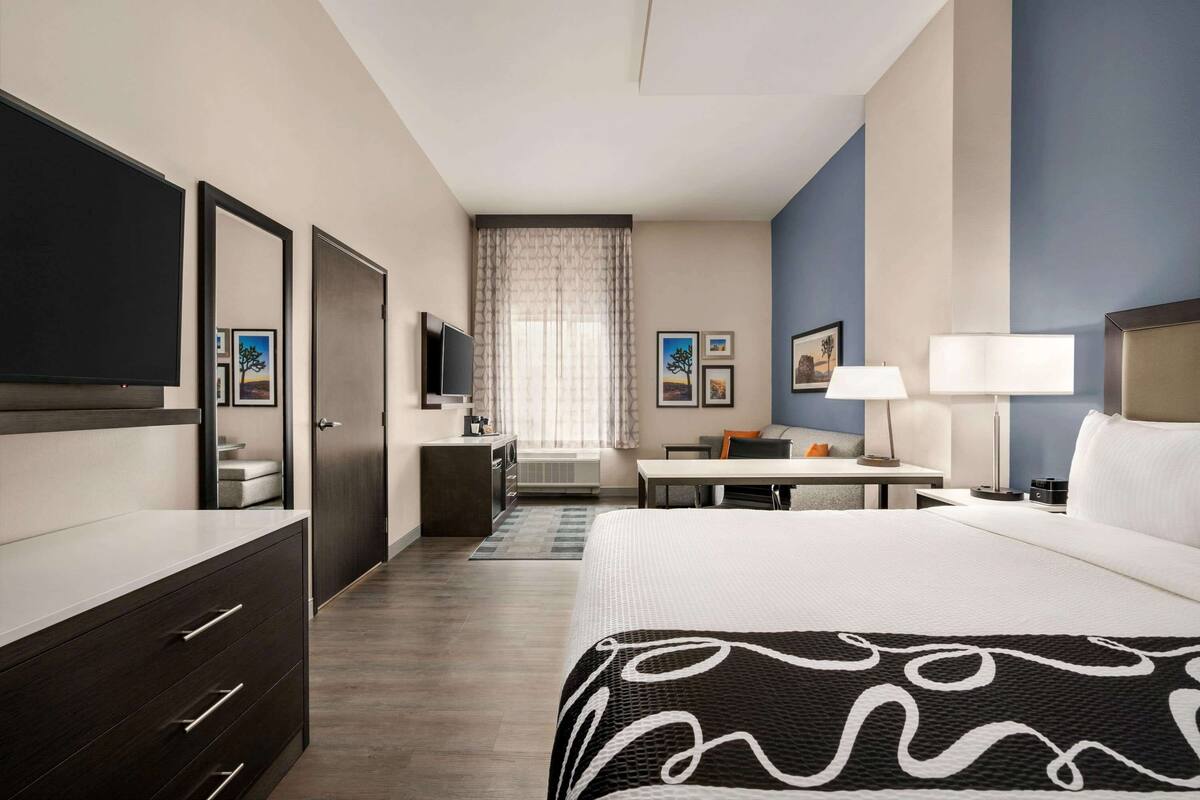 A hotel room with a large bed, a desk, a TV, a wardrobe, and a window with curtains.