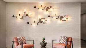 Una habitación moderna con dos sillas, una mesita con una planta y una lámpara fijada a la pared.