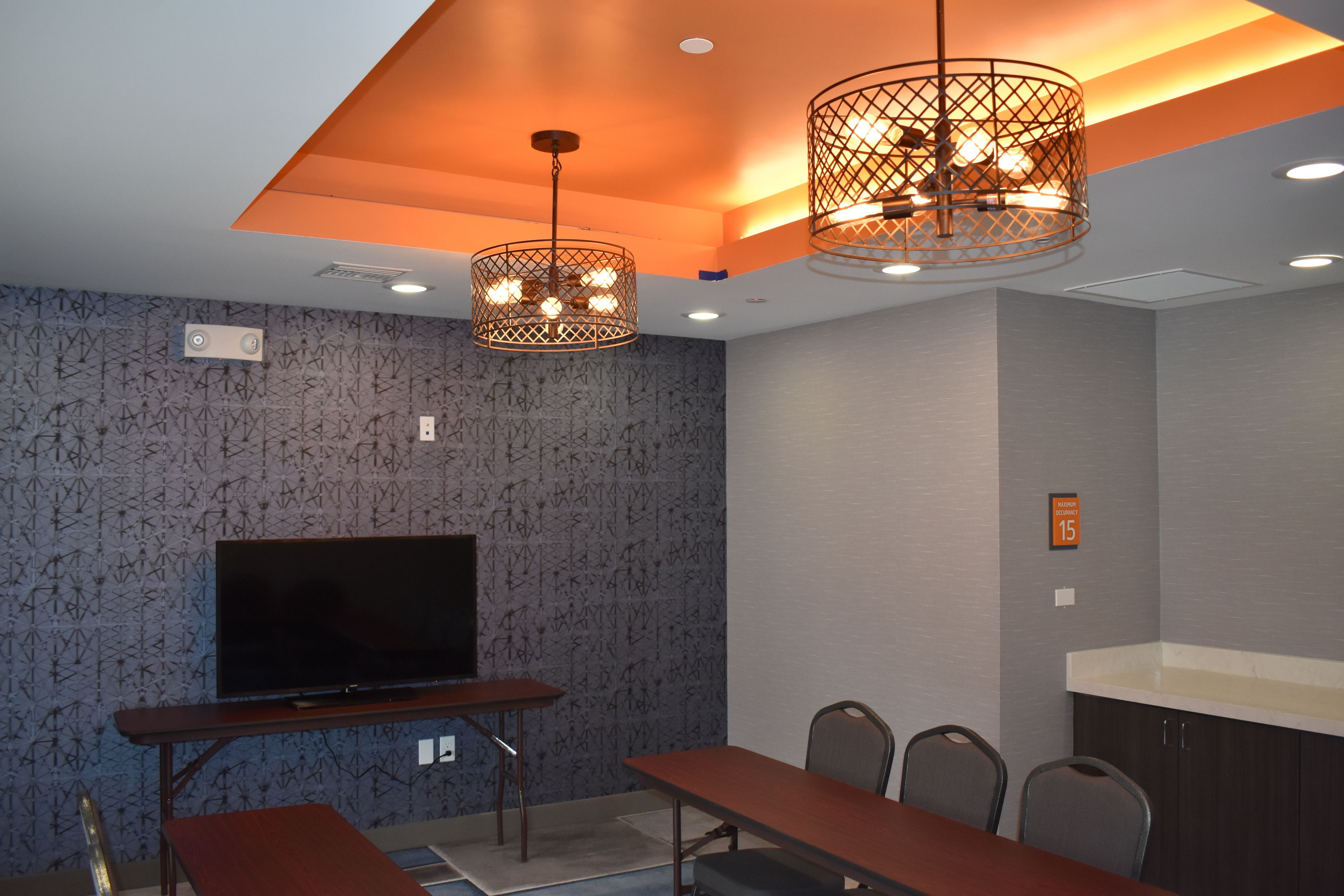 A conference room with a large flat-screen TV, a wooden table, four chairs, and two pendant lights with a geometric design.