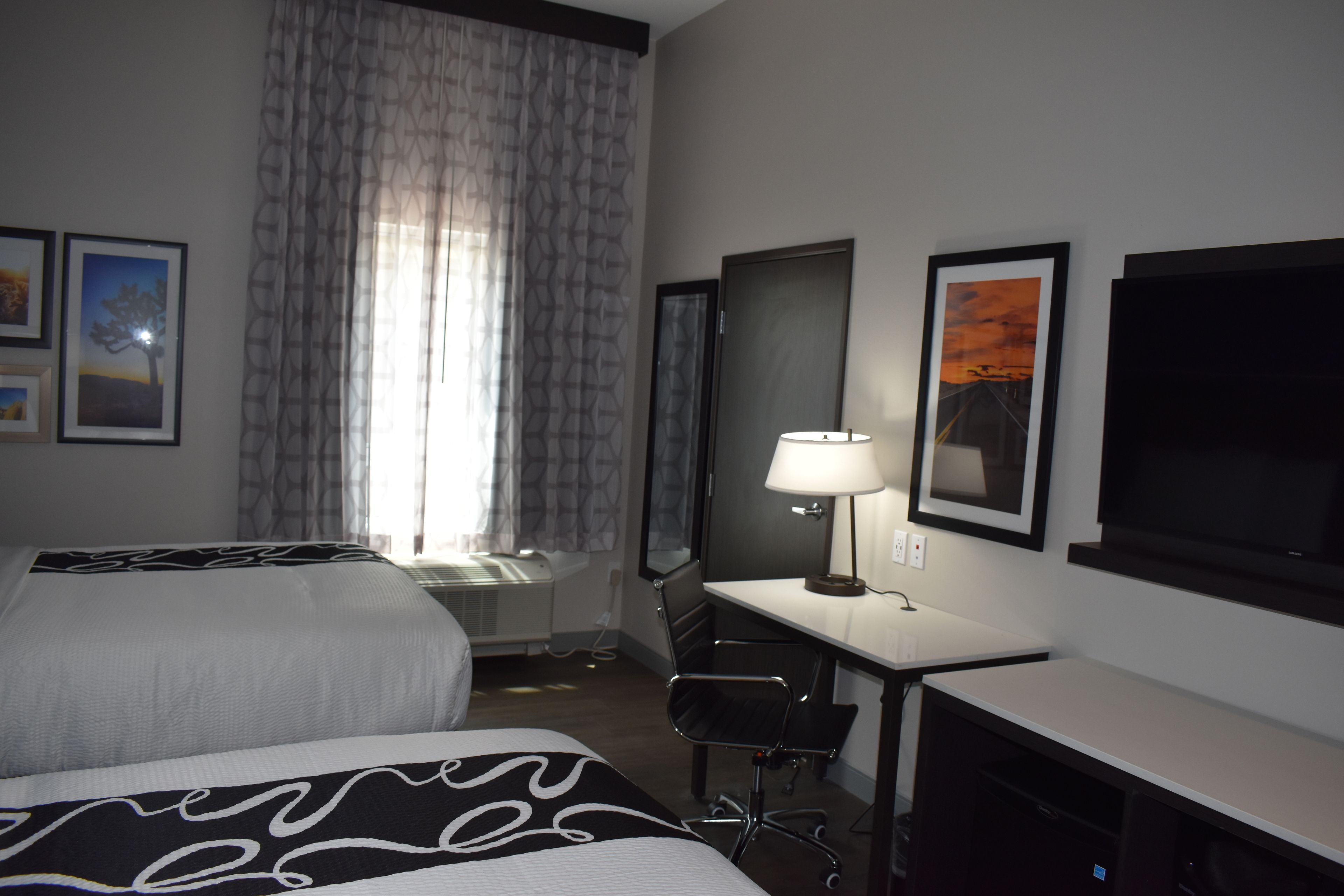A hotel room with two beds, a desk with a chair, a TV, and framed pictures on the wall.