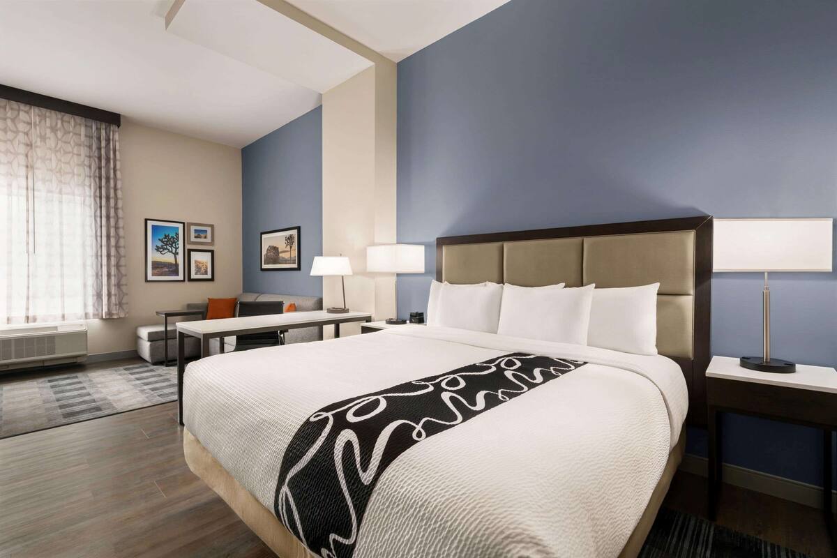 A hotel room with a large bed, a desk, a chair, a lamp, and a window with curtains.
