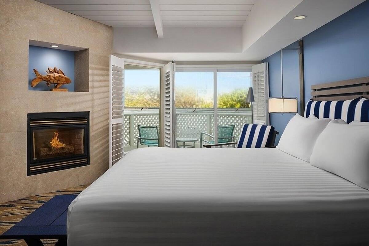 A bedroom with a fireplace, a balcony with chairs, and a bed with striped pillows.