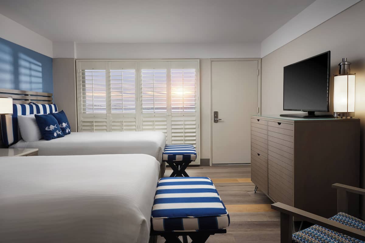 A hotel room with two beds, a TV, a dresser, and a bench.