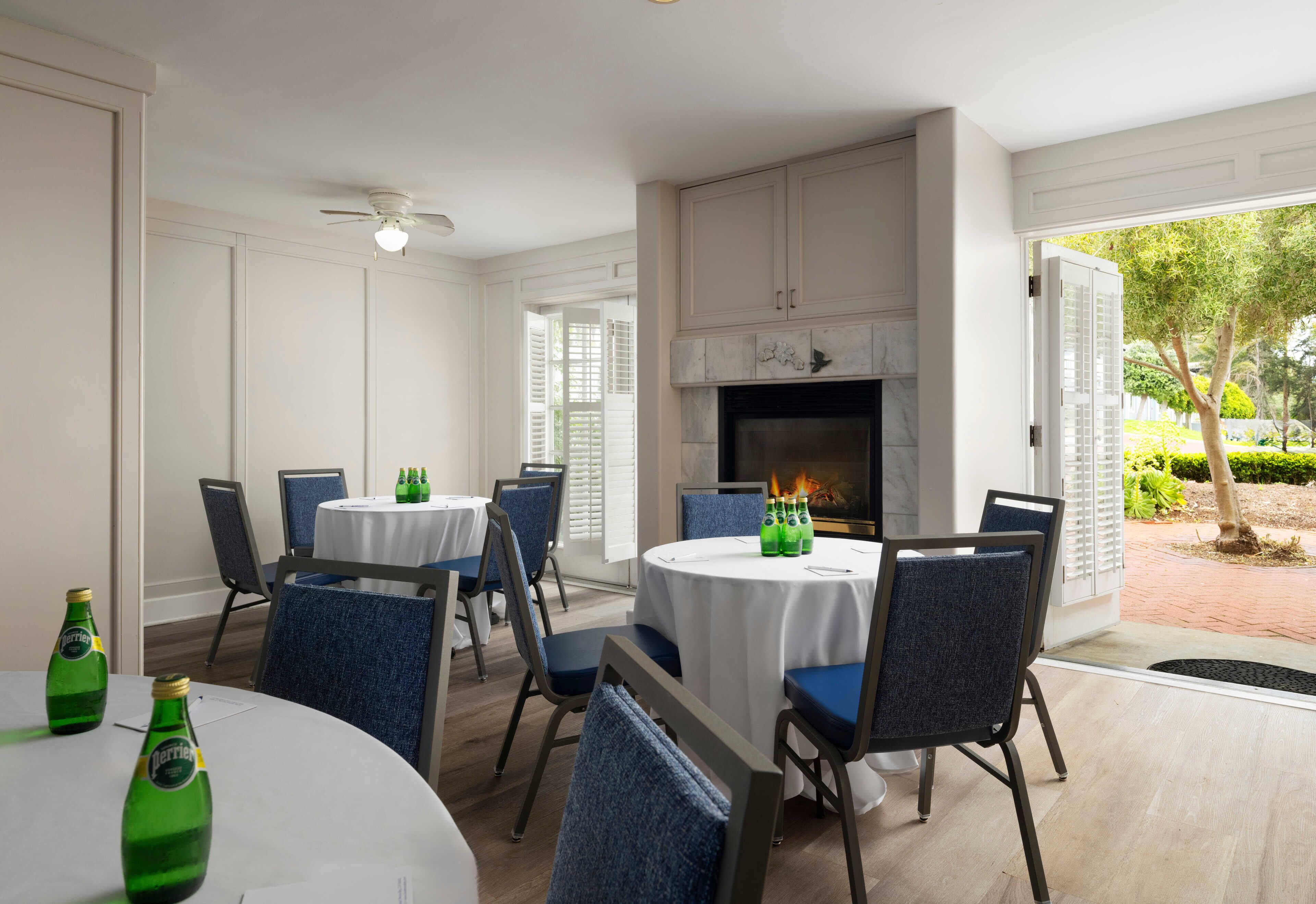 A dining area with round tables, blue chairs, and a fireplace.