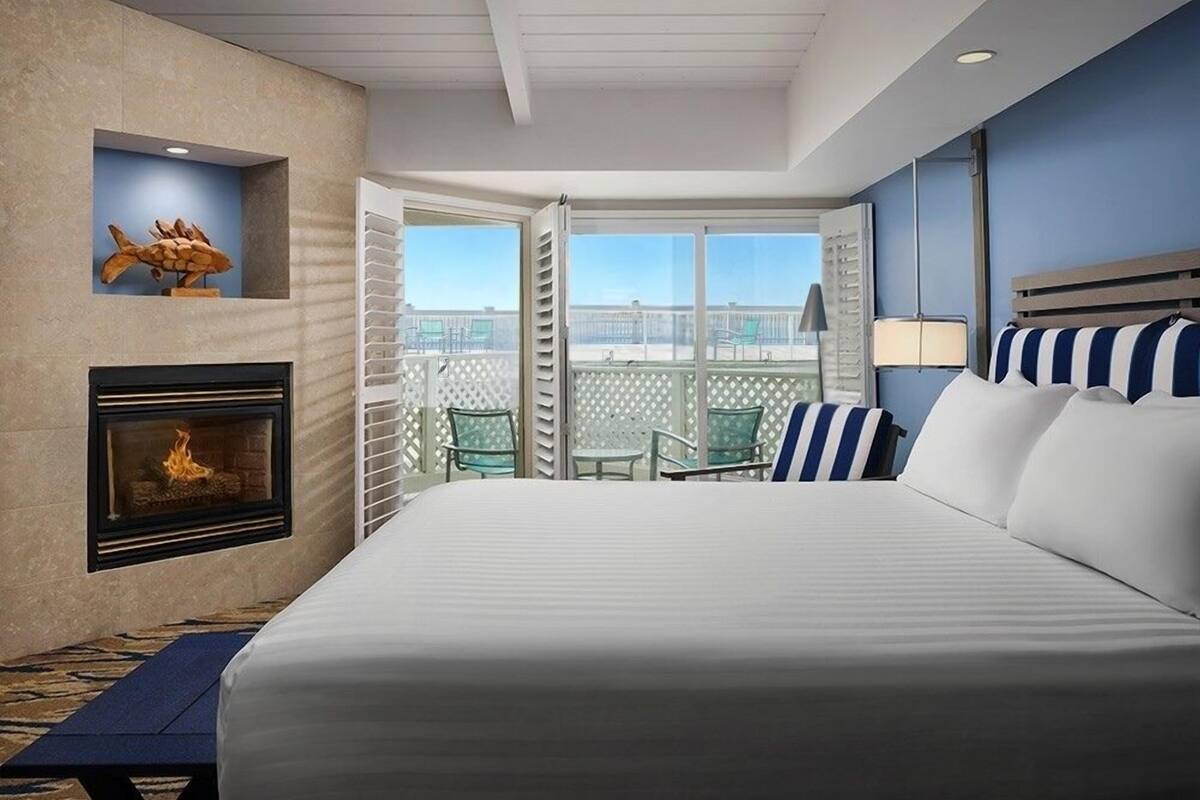 A hotel room with a fireplace, a bed with striped pillows, a balcony with chairs, and a view of the city.