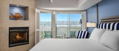 Habitación de hotel con chimenea, cama con almohadas a rayas, balcón con sillas y vistas de la ciudad.