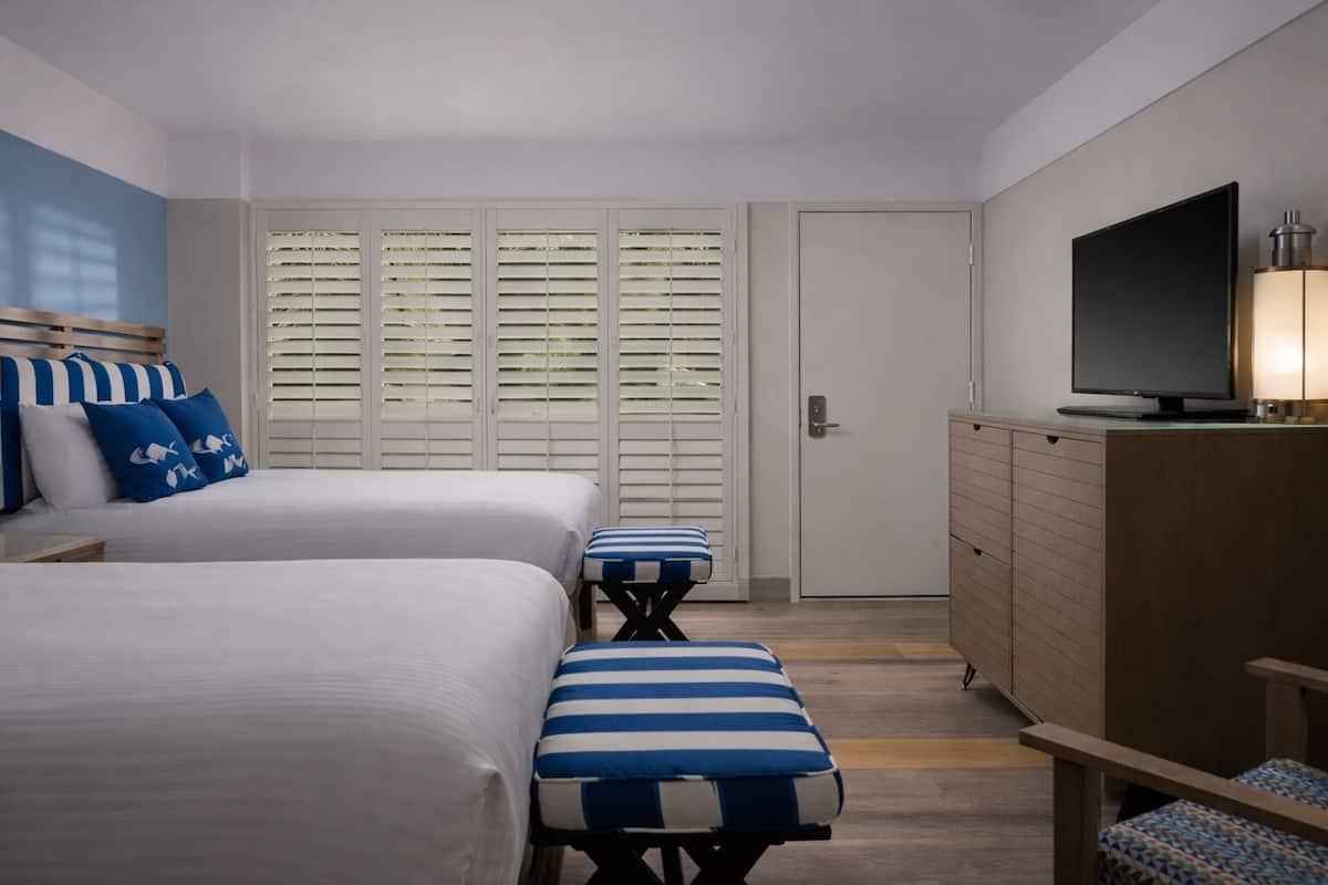 A hotel room with two beds, a TV, a dresser, and a window with blinds.