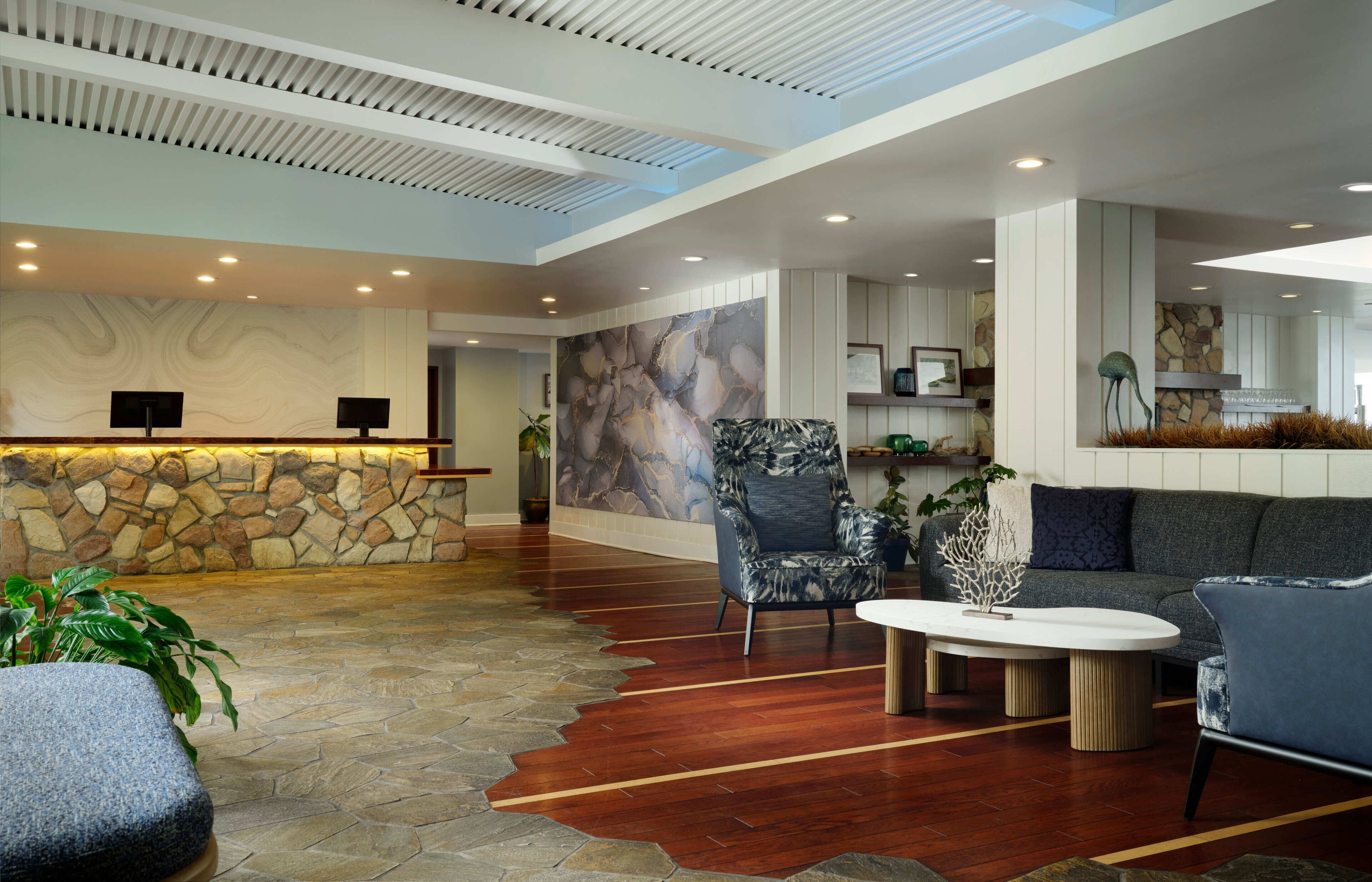 A spacious lobby with a stone reception desk, comfortable seating, and a modern ceiling design.