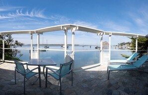 Enjoy a serene sea view from this outdoor patio with a pergola, table, and comfortable seating for two.