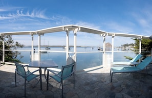 Enjoy a serene sea view from this outdoor patio with a pergola, table, and comfortable seating for two.