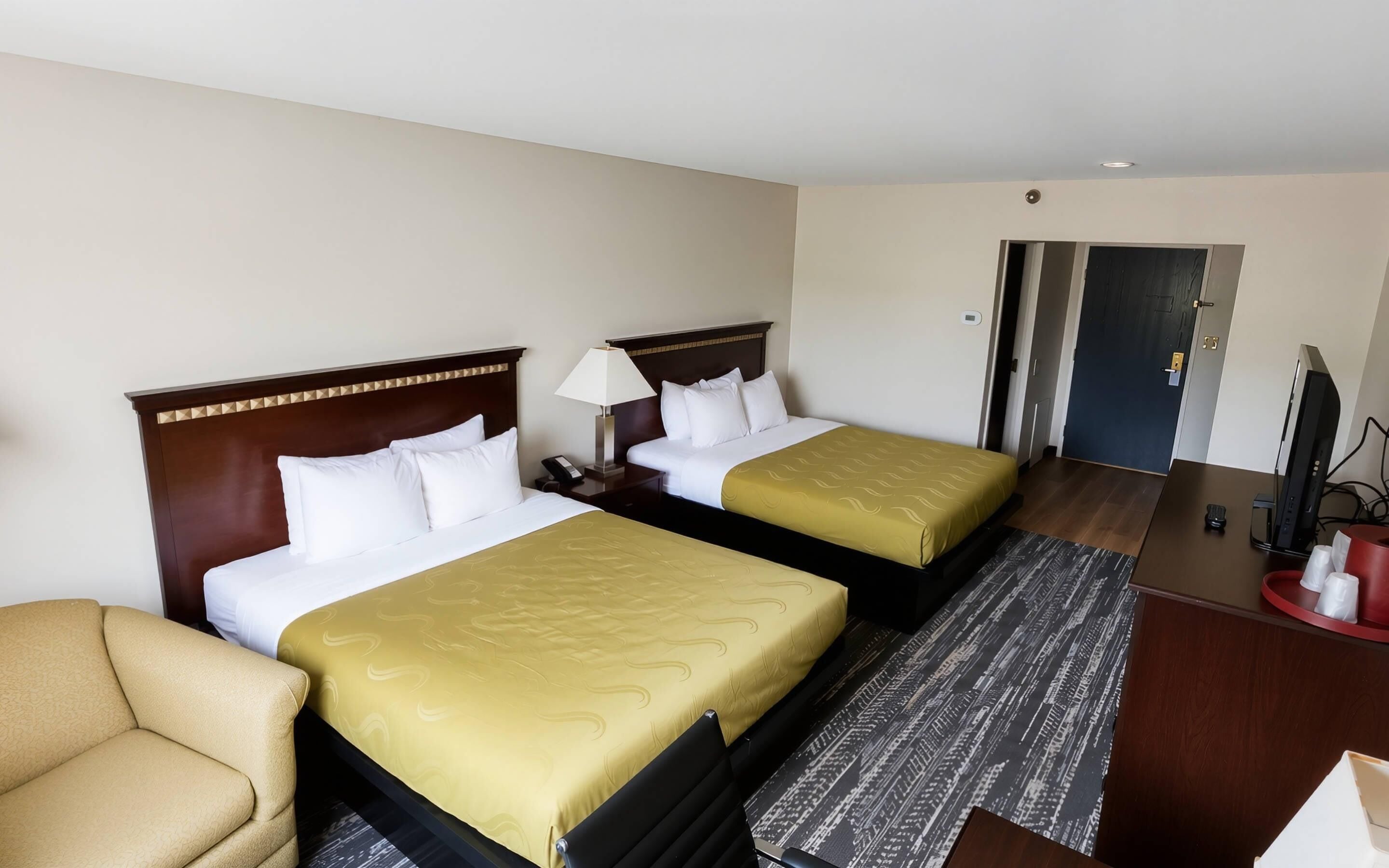 A hotel room with two beds, a desk, a chair, and a television.