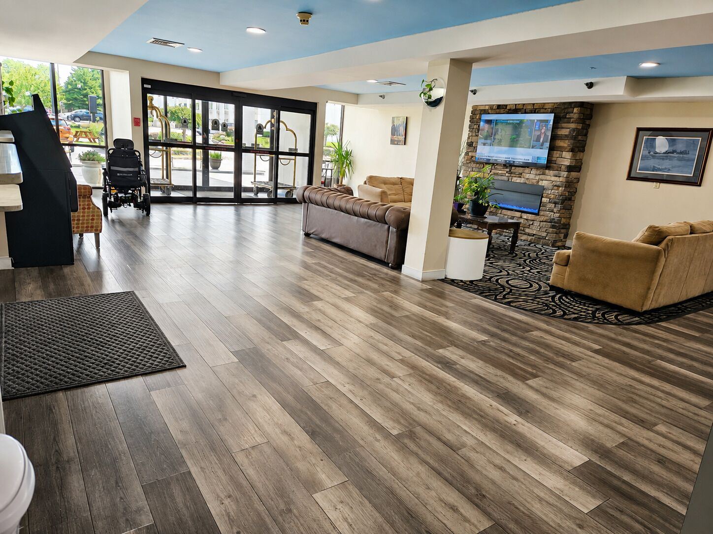 A spacious lobby with a wooden floor, a wheelchair, a sofa, and a television mounted on a stone wall.