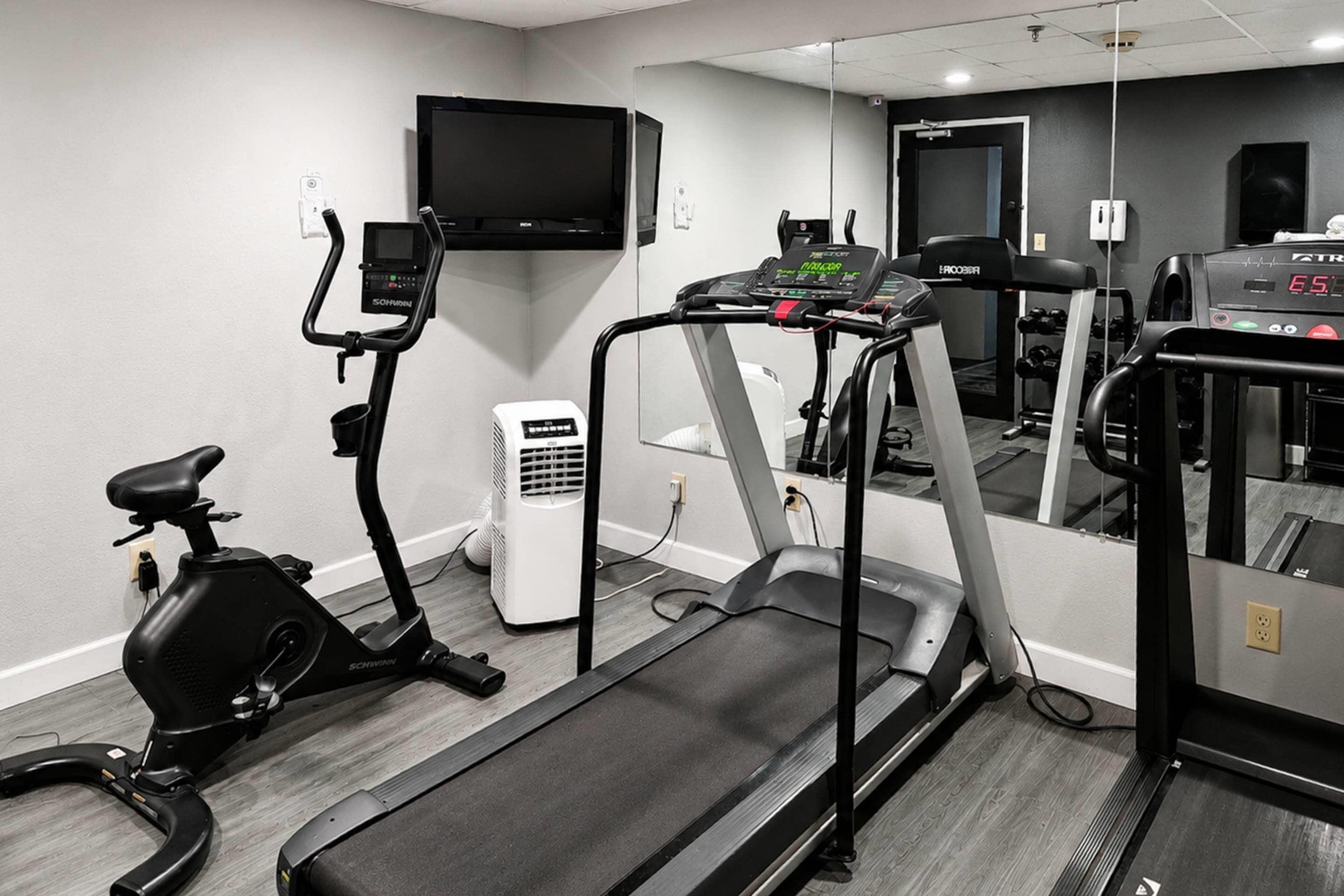 A gym with a treadmill, stationary bike, and a mirrored wall reflecting exercise equipment.